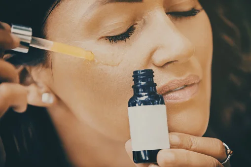 Close up of mid adult woman applying face serum on her face.